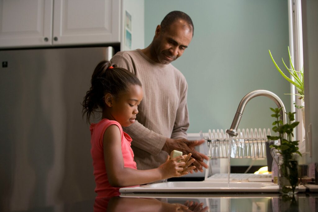 A father teaching responsibility to his daughter in the form of washing dishes.